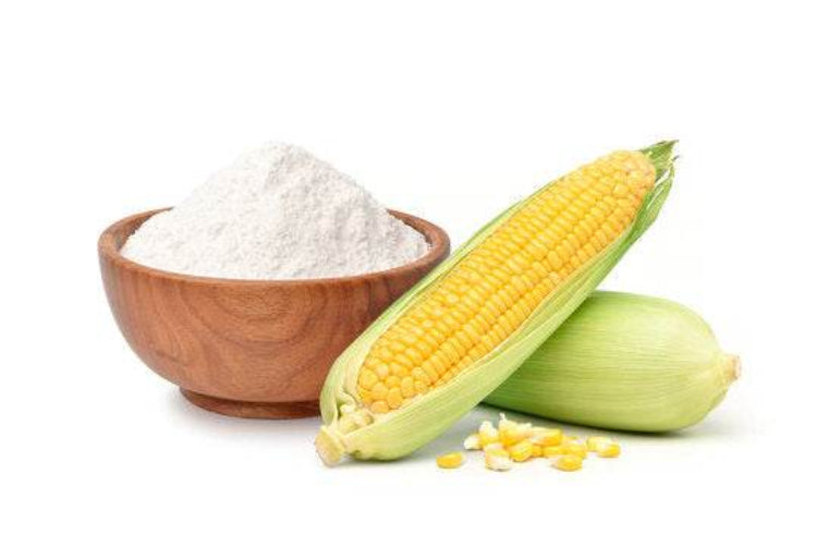Corn kernels and a bowl of corn starch on a white background