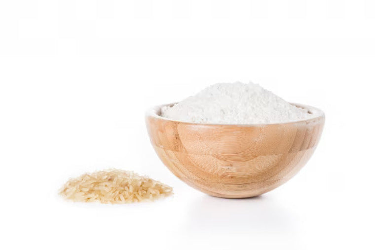 A wooden bowl filled with rice flour, with a small amount of rice flour also scattered beside the bowl on a white background.