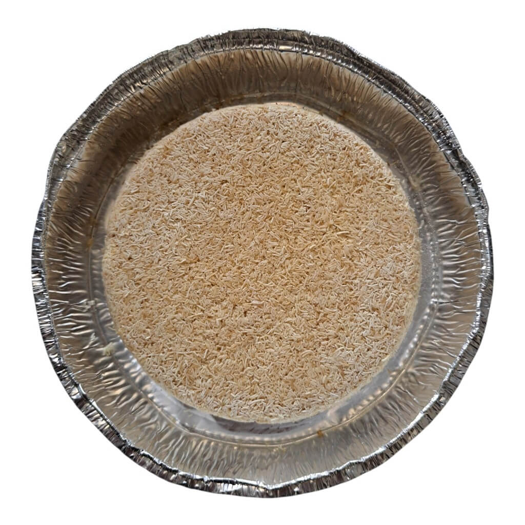 A round aluminum pie dish filled with a light tan granular material, photographed from directly above on a plain white background.