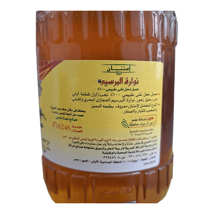 A large plastic bottle of honey with a ribbed shoulder design, filled with golden honey and featuring a large yellow label with Arabic text.